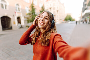 Selfie time! Young woman with headphones taking selfie and blogging while walking through the city...