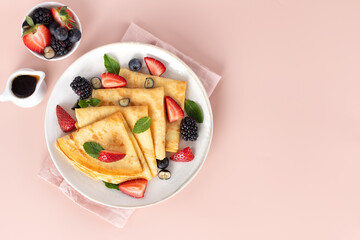 French breakfast crepes with strawberries, blackberries and maple syrup on pink background. Top view