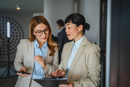 two diverse female colleagues review together document files in hallway