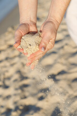 Female hands picking up a handful of sand from the beach. Summer holidays and vacation concept.