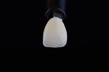 Close up shot ultra thin dental zirconium crown is held with tweezers with black background.