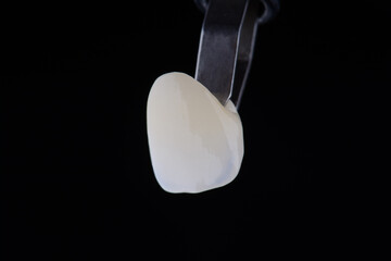 Close up shot ultra thin dental zirconium crown is held with tweezers with black background.