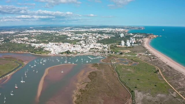 Beautiful aerial view of alvor, portugal, showcasing the cityscape, harbor filled with boats, a long sandy beach, and the clear blue waters of the atlantic ocean. Aerial view praia de Alvor