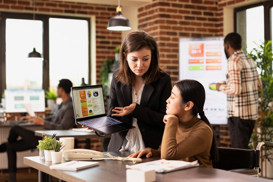 Fototapeta Professional marketer using the internet to display advertising strategies, analyzing client data in modern workspace. Two female coworkers concentrating on business analytics on laptop.