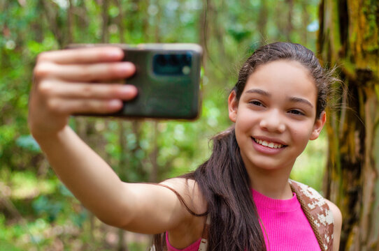 Smiling teenage girl taking a selfie in the forest with smartphone
