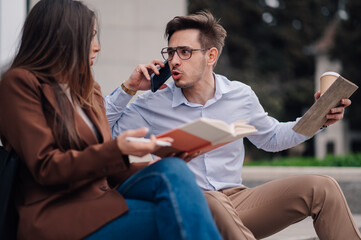 Stressed businessman multitasking with phone, books, and coffee, talking to colleague