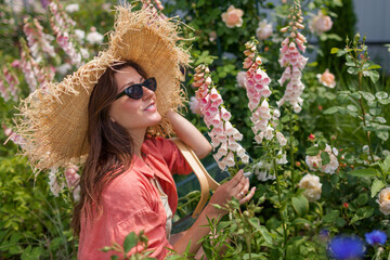 Portrait of stylish woman gardener admiring foxglove flowers picking stems in summer garden. Peachy pink digitalis in blossom