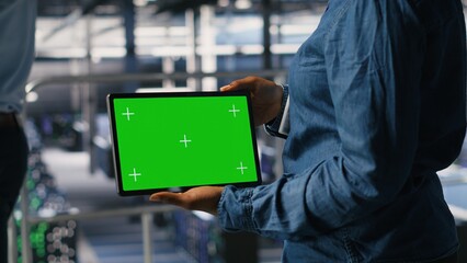 Close up of IT experts using chroma key device to analyze neural networks outputs. Data center admin uses green screen tablet next to colleague reviewing AI visualization in blurry background