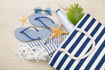 Blue beach bag with summer accessories on wooden background, top view