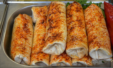 Delicious spiced wraps are arranged neatly in a metal serving tray, ready for customers. Seasoned with paprika and sesame, they reflect traditional preparation and inviting street food appeal