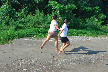 Two teenage girls sprint joyfully across the sandy path near the campsite, surrounded by lush...