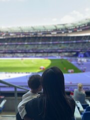 Behind view of a mother and her son enjoy watching sport at stadium. Quality time and generational sport supoorters in the crowd