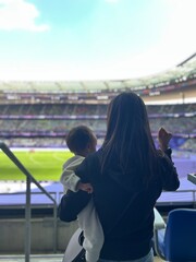 Behind view of a mother and her son enjoy cheering sport at stadium. Quality time and generational sport supoorters in thr crowd