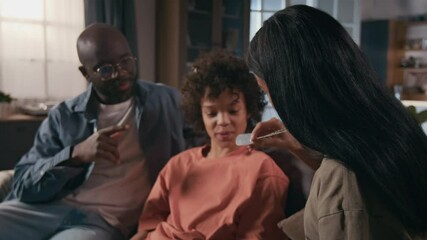 Medium shot of cheerful, proud young female soldier in khaki military t-shirt relaxing on couch with African American husband and son after returning from service, showing identification tag