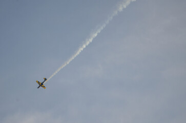 Aerobatic yellow plane loops in blue sky with smoke trail