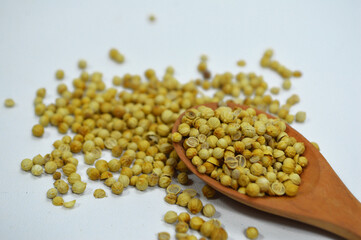 Wooden spoon filled with organic Coriander seeds (Coriandrum sativum), placed on a pile of whole...