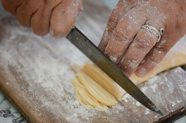 Hands slicing pasta dough on floured wooden board