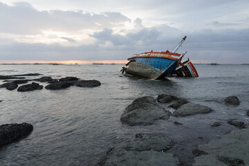 Old wrecked fishing boat at shore of Ang Sila Village, Saensuk Sub-district, Chonburi Province of thailand with sunset skyline suite for concept of end of journey, natural disaster, storm and surge.