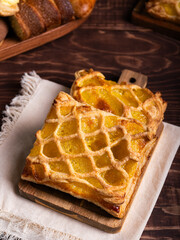 Two golden-brown pastries with a lattice crust and a vibrant yellow filling, rest on a wooden board