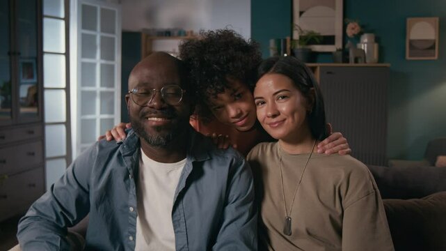 Medium portrait of happy female army officer in khaki uniform t-shirt, with identification tag sitting on couch with African American husband and biracial son, looking at camera, smiling - Powered by Adobe