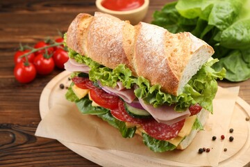 Tasty baguette sandwich with ham and vegetables on wooden table, closeup
