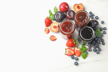 Different sweet jams in jars and ingredients on white marble table, flat lay. Space for text