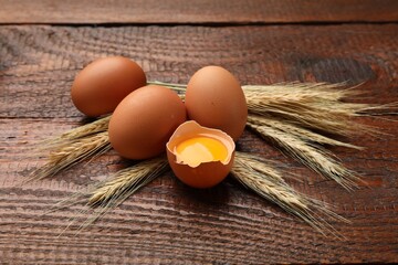 Raw eggs and spikes of wheat on wooden table, closeup