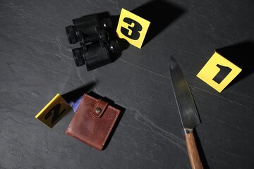 Forensic expert. Yellow evidence markers, knife, binoculars and wallet on black table, flat lay