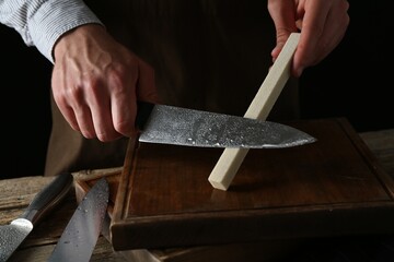Man sharpening knife with sharpener on wooden table, closeup