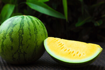 Whole and cut yellow watermelons on wicker table outdoors, closeup