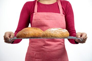 Woman in red apron holding wire rack with two freshly baked crusty loaves of bread, showing golden brown color and homemade rustic texture