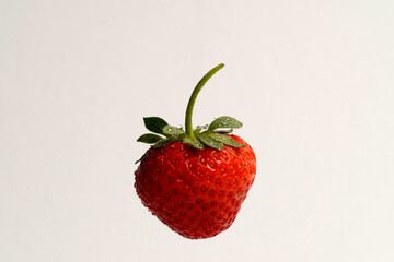 Single fresh strawberry with stem and water droplets floating on a white background. Macro close-up of vibrant red berry. Clean eating and fruit freshness concept.

