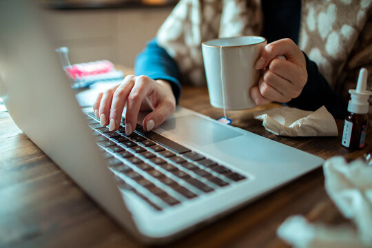 Sick woman working from home with tea and laptop