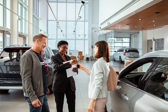 Couple receiving car keys from dealership saleswoman at showroom