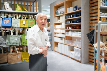 In a stylish Japanese boutique filled with home goods, a Japanese man in his late 70s, wearing a white shirt, browses items with a relaxed expression, appreciating the carefully arranged displays.