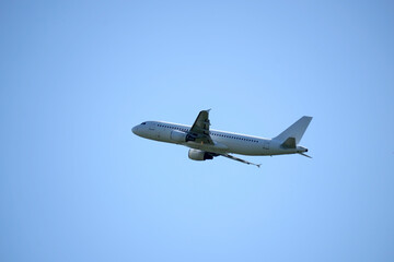 White commercial airplane flying in a clear blue sky, viewed from below and side, showing wings, engines, and tail.

