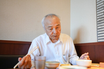 In a traditional Japanese diner, a Japanese man in his late 70s wearing a white shirt sits at a wooden table, enjoying a set meal of classic Japanese dishes served with rice and miso soup.