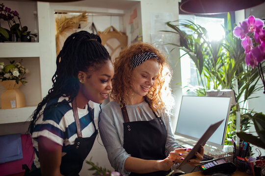 Two female florists using a digital tablet while working on flower arrangements in their shop