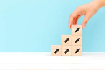 Hand holding wooden cube blocks print up arrow on blue background with space, investment, income, inflation, business growth, economic improvement concepts