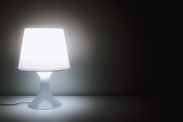 Glowing lamp night light on table in a dark room with space. Vintage effect style picture. Living, home and office interior concept