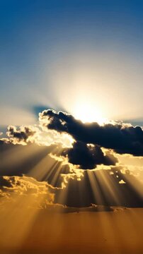 Golden sunlight streams through dark clouds in a blue sky, creating ethereal beams and a dramatic atmospheric landscape
