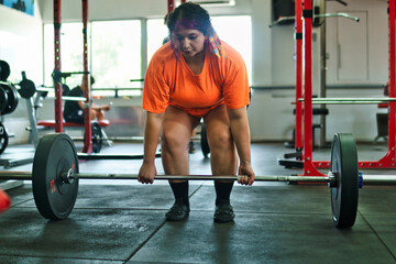 View of a beautiful, overweight young Latina lifting weights and working out at a gym. Positively, she's pushing herself to the limit. She's improving and feeling better.