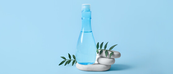Bottle of micellar water, stones and leaves on blue background