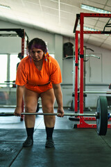 View of a beautiful, overweight young Latina lifting weights and working out at a gym. Positively, she's pushing herself to the limit. She's improving and feeling better.