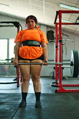 View of a beautiful, overweight young Latina lifting weights and working out at a gym. Positively, she's pushing herself to the limit. She's improving and feeling better.