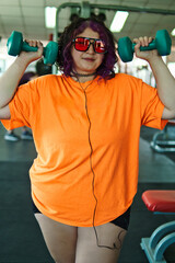 Beautiful young overweight Latina posing and exercising with weights and listening to music, wearing retro glasses and a Discman in a retro-style gym, working hard, very happy. Health and improvement.