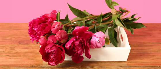 Tray with beautiful peony flowers on wooden table against pink background