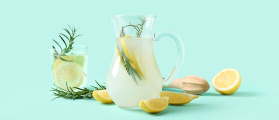 Jug and glass of fresh lemonade with rosemary on turquoise background