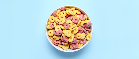 Bowl with corn cereal rings on blue background, top view