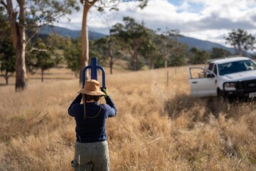 female farmer driving steel posts with a post driver on a farm putting up a steel post fence with high tensile wire in australia women in agriculture in spring